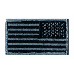 Embroidered emblem featuring a U.S. Flag design. Measures 3 3/8 inches by 2 inches. Black and silver colors. Made of plastic. Attaches by sewing onto fabric. Suitable for uniform, bag, or apparel identification.