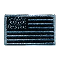 Sew-on embroidered emblem featuring a U.S. Flag design. Measures 3 3/8 in x 2 in. Constructed with a plastic base and black/silver thread. Suitable for attachment to clothing, bags, or uniforms for identification or display.