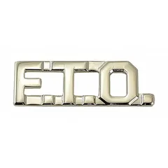 This metallic rank insignia displays the F.T.O. (Field Training Officer) designation. It is constructed of silver-finished metal and measures 3/8 inch. The insignia attaches to uniform fabric via a clutch pin fastener. Typical use includes identification of training officers in law enforcement or security uniforms.