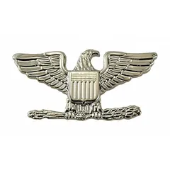 This metallic insignia features a silver eagle design representing the rank of Colonel. Measuring 3/4 inch, it is made of metal and attaches via a clutch pin. Commonly used on military or ceremonial uniforms to denote rank.