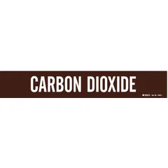 This adhesive pipe marker features a brown background with white legend reading 'Carbon Dioxide' and fits pipe outer diameters from 2-1/2 to 7-7/8 inches. It is supplied without arrows and is used to identify carbon dioxide piping in industrial facilities, aiding in safety and compliance with pipe-identification standards.