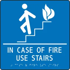 Adhesive sign with white/blue background and raised Braille text. Nominal size 9 in x 9 in. Mounts directly to walls or doors. Used to indicate emergency exit routes and instruct building occupants to use stairs instead of elevators during a fire.