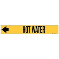 Adhesive pipe markers on a roll for identifying hot water piping systems. Yellow background with black legend and directional arrows. Each marker fits pipe outer diameters of 1-1/2 to 2 inches. Supplied in rolls of 25 markers